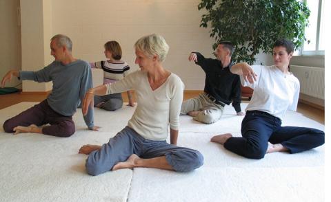 several people seated on a white mat on the floor of a brightly lit room 