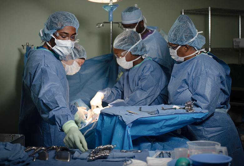 surgeons and technicians wearing blue scrubs working on a surgery in a hospital setting